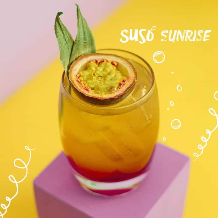 Suso Sunrise cocktail on yellow background with passion fruit half in it as a garnish